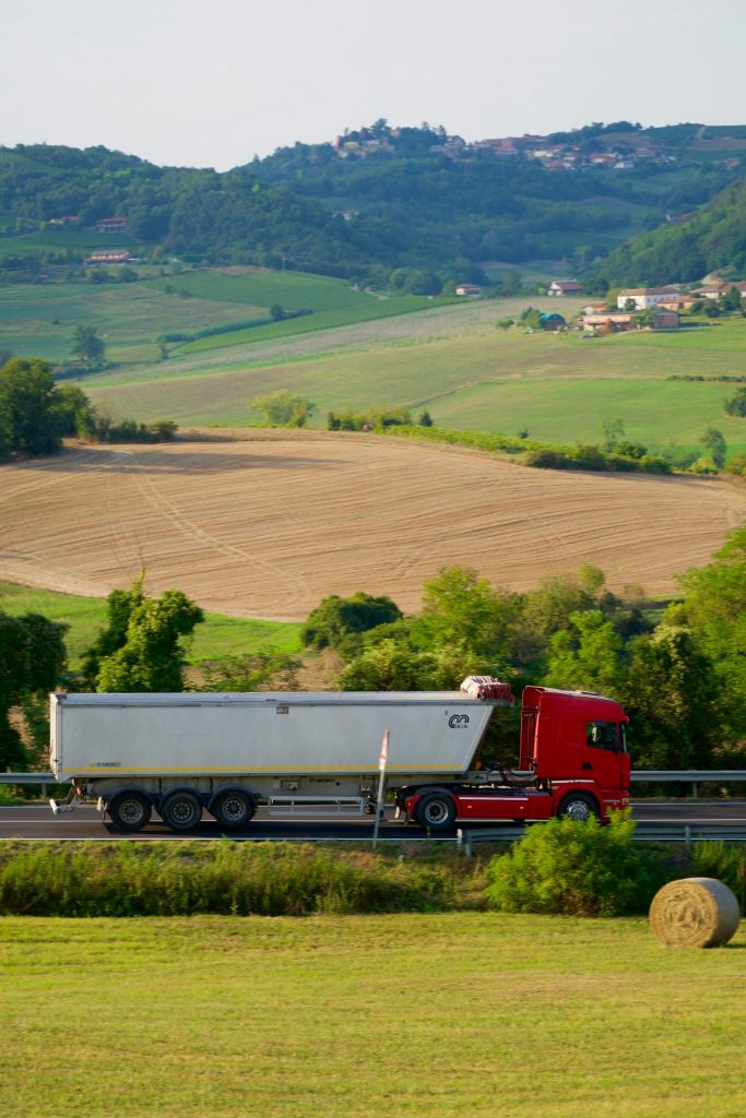A red truck driving down a road next to a lush green field
